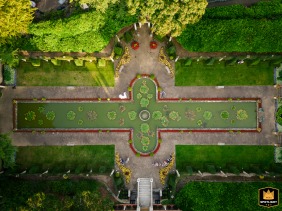 At The Italian Villa in Dorset, UK, the bride and groom pose playfully near the pond for a drone portrait, amid the elegant landscape captured from above, showcasing their lighthearted spirit amid the villa’s picturesque grounds.